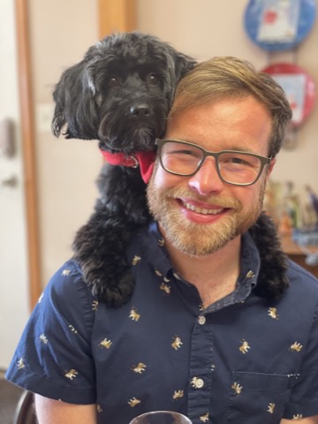 Brad Burch with a small black dog resting across his shoulders